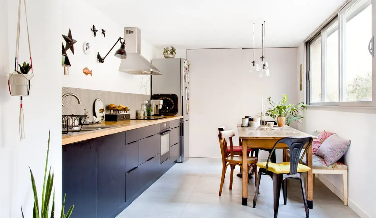Cuisine salle à manger en longueur avec meubles sombres, plan de travail en bois, table en bois et banquette.