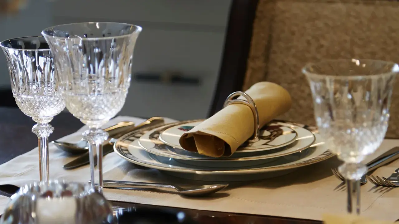 Verre à pied taillé, assiettes décorées, serviette en tissu joliment pliée : une table dressée pour le service à la française.