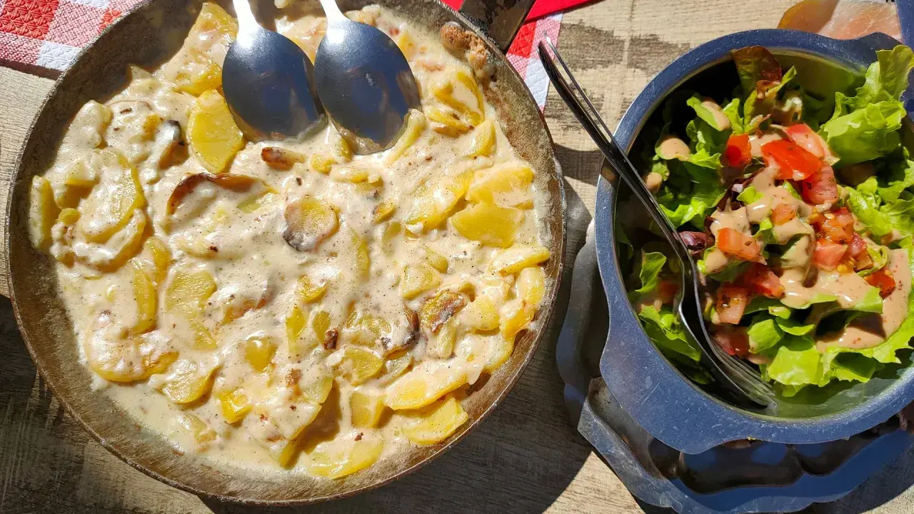 Plat de pommes de terre crémeuses, une spécialité auvergnate, servi dans une poêle avec une salade fraîche.