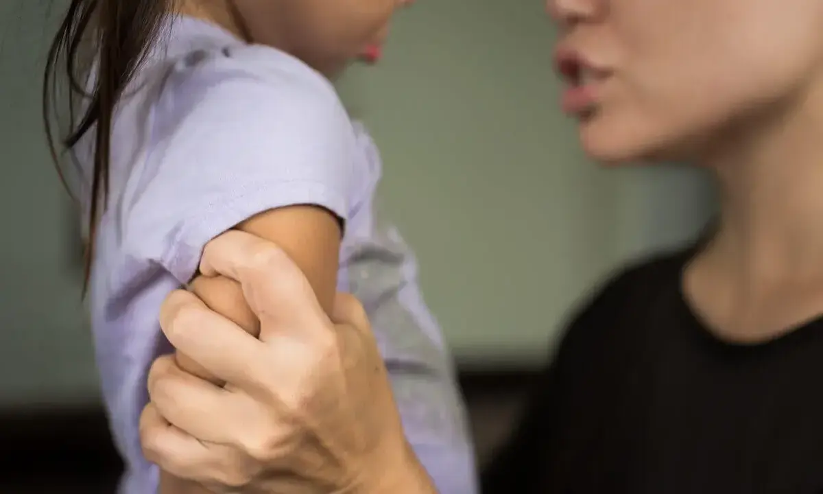 Eine Erzieherin hält ein Kind am Arm fest, während sie spricht. Die Frage, ob eine Erzieherin ein Kind festhalten darf, ist komplex.