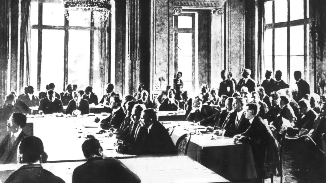 Männer in Anzügen sitzen an langen Tischen in einem prunkvollen Saal. Dies ist die Unterzeichnung des Versailler Vertrags, der den Ersten Weltkrieg beendete.
