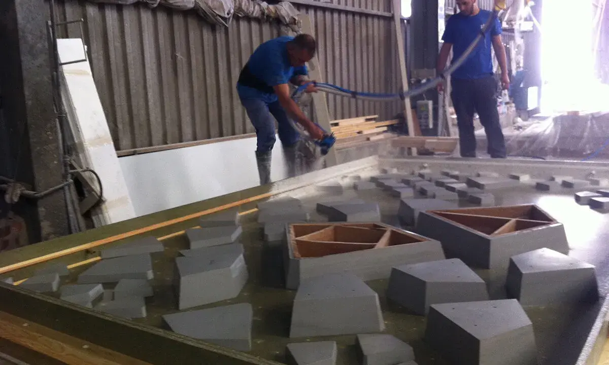 Dos operarios trabajan con material GRC en un taller, uno rocía con una manguera y el otro supervisa.