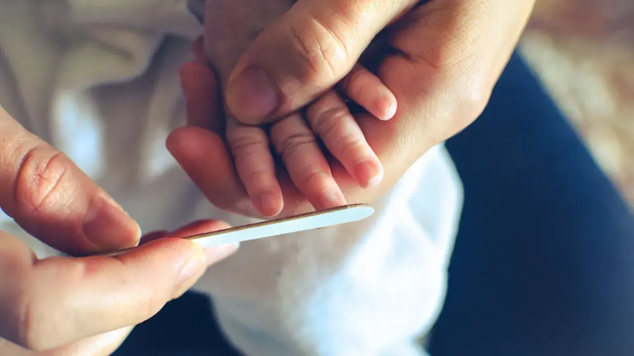 Mani adulte limano delicatamente le unghie di un neonato, un momento di cura che mostra quando si possono tagliare le unghie ai neonati.