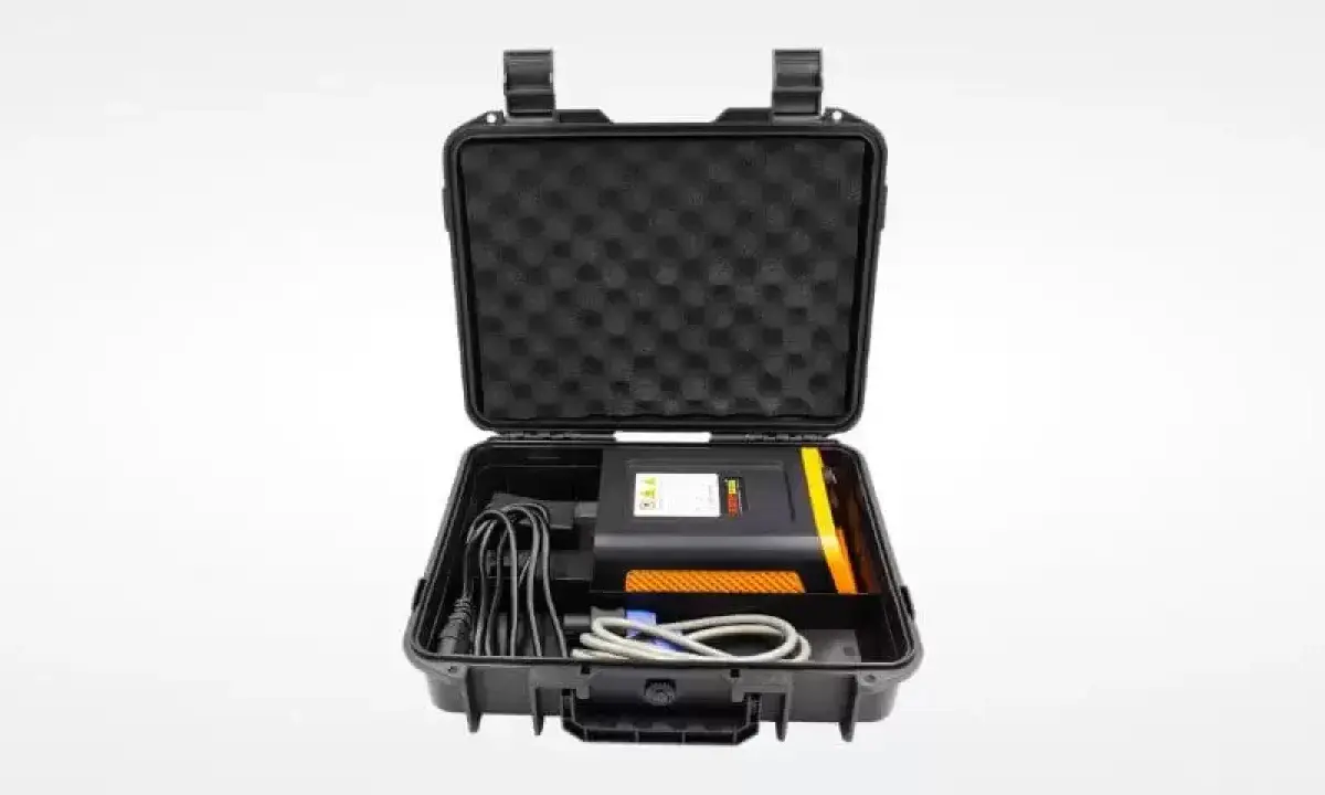 Estuche negro abierto con un dispositivo electrónico negro y naranja, cables y espuma protectora. Ideal para un sacabollos profesional.