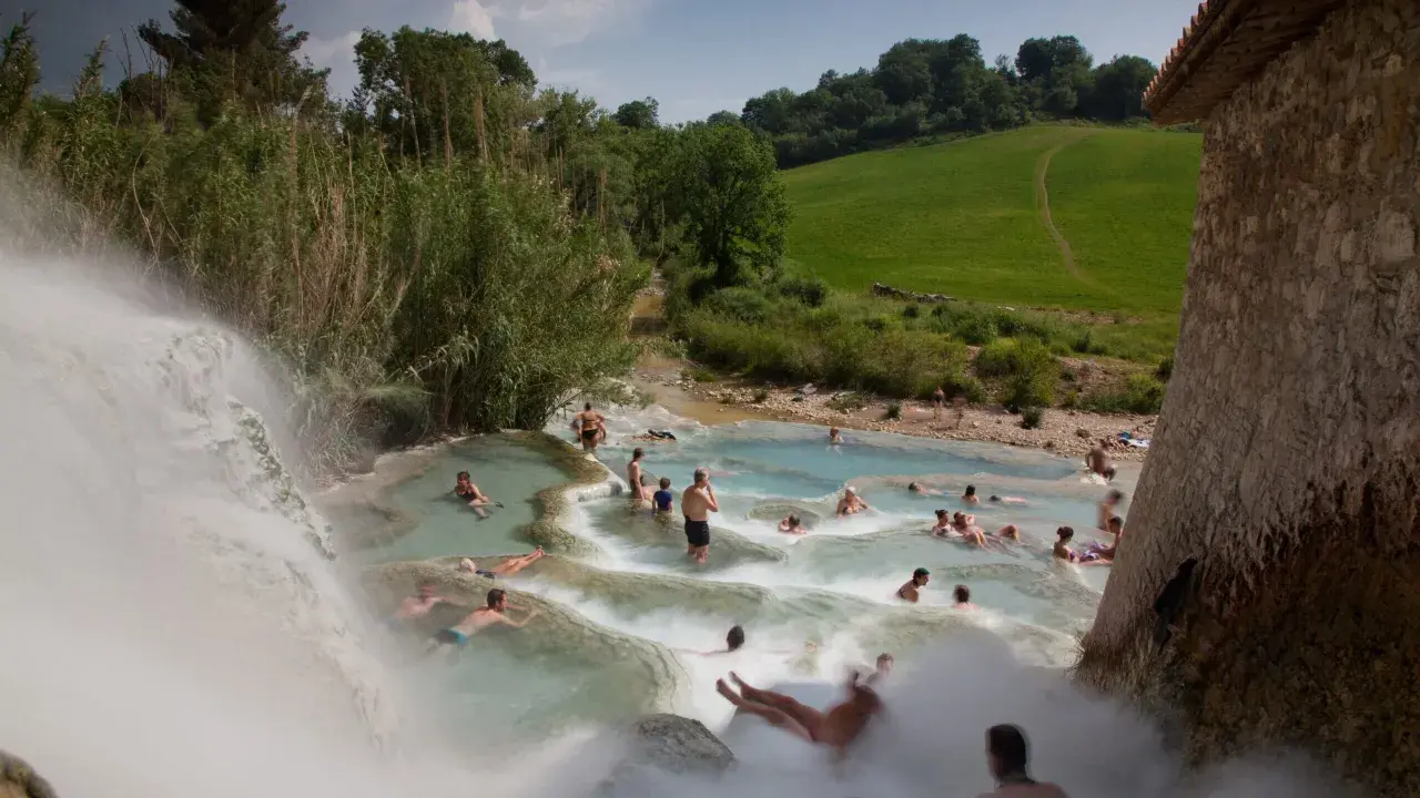 Persone si rilassano nelle cascate naturali delle **Terme di Saturnia**, immerse nel verde della campagna toscana.