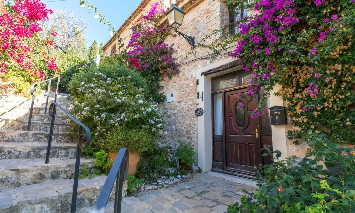 Escaleras de piedra adornadas con buganvillas y flores blancas, que llevan a la entrada de una casa de piedra. Un ejemplo de los pueblos bonitos de Alicante.