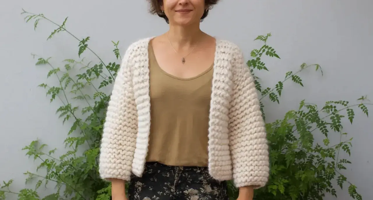 Mujer sonriente luce una chaqueta dos agujas tejida a mano, ideal para aprender paso a paso.
