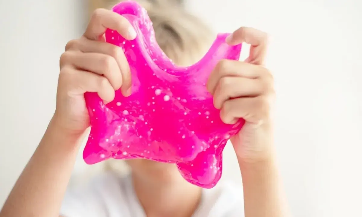 Dziecko bawi się różowym slime, który wygląda jak z przepisu na domowy slime.