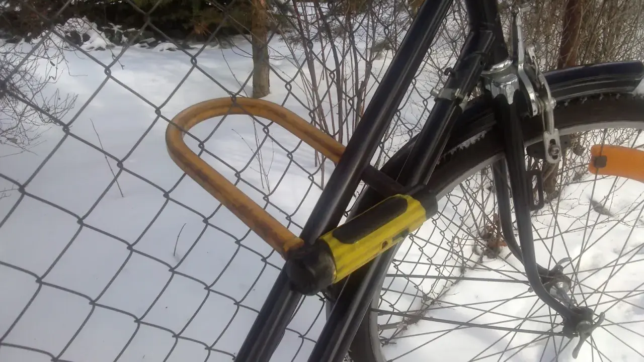 Żółta kłódka U-lock zabezpieczenie roweru przed kradzieżą, przypiętego do siatki w zimowy dzień.