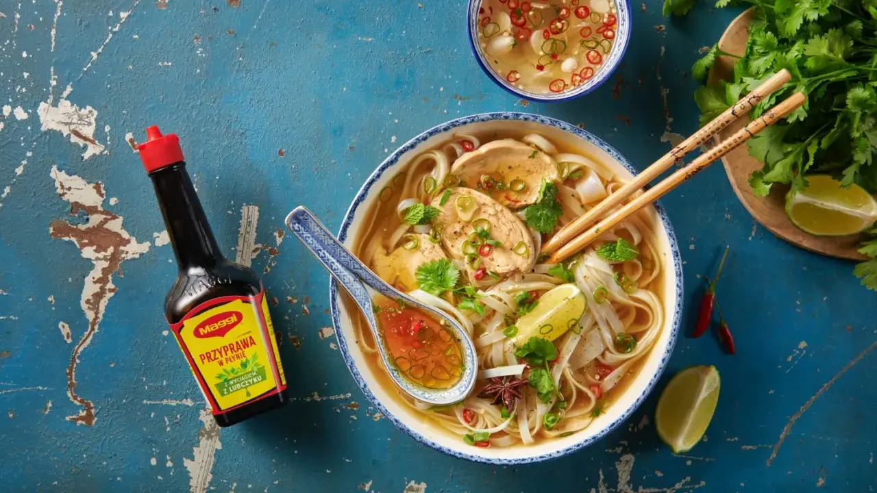 Aromatyczna zupa pho z kurczakiem, makaronem ryżowym, limonką i świeżą kolendrą. Obok butelka przyprawy Maggi.