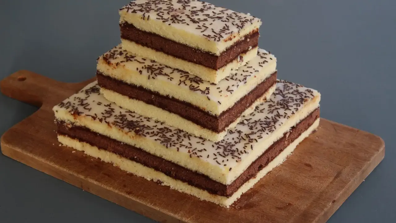 Trois parts de napolitain sans gluten empilées sur une planche en bois, garnies de vermicelles au chocolat.