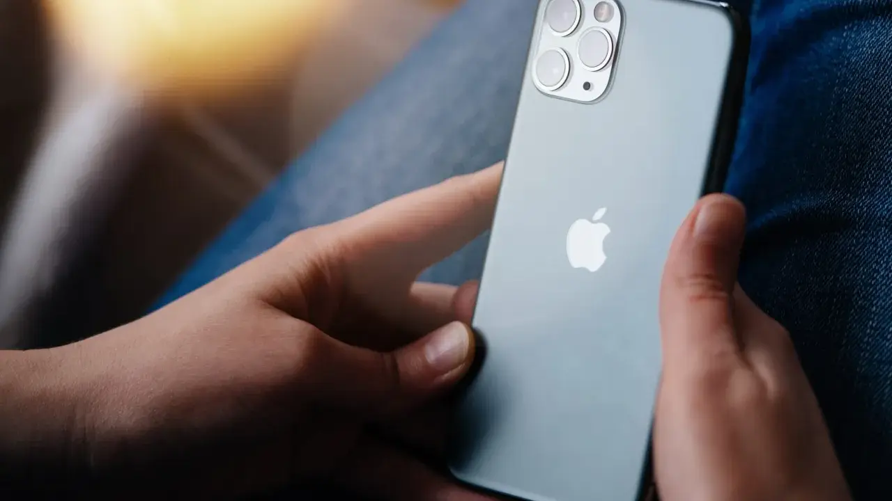 Dłonie trzymające szare iPhone'a z widocznym logo Apple i modułem aparatów.