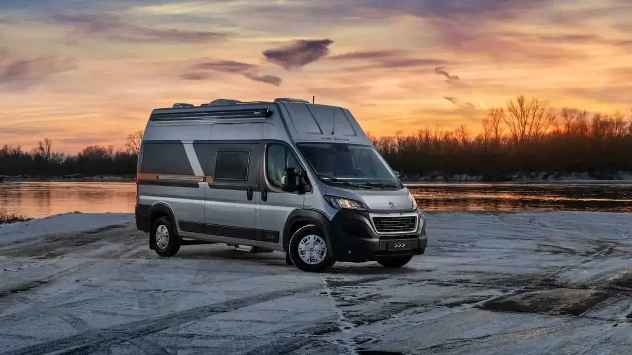 Srebrny kamper Globe-Traveller na tle zachodzącego słońca nad rzeką. Idealny wybór, jeśli zastanawiasz się, jaki kamper dla 2 osób sprawdzi się najlepiej na zimowe wyprawy.