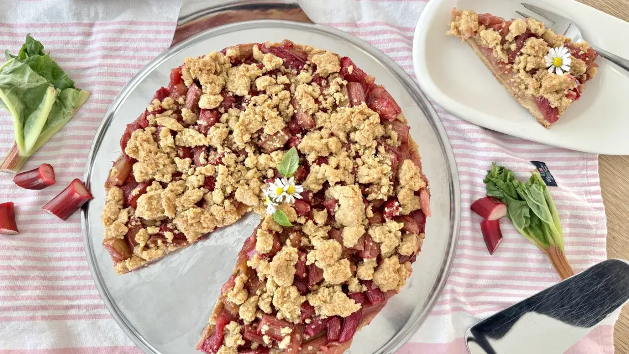 Ein köstlicher Rhabarber Streuselkuchen mit frischem Rhabarber und knusprigen Streuseln, garniert mit kleinen Gänseblümchen.