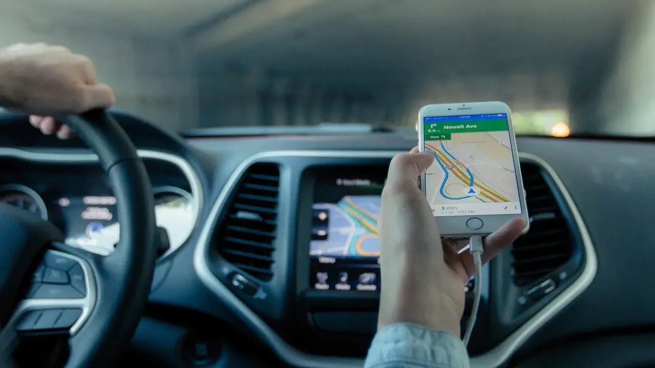Mano al volante, móvil con mapa GPS mostrando cómo funciona un localizador GPS para coche.