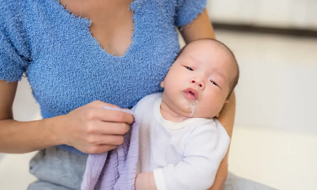 Un neonato con rigurgito, tenuto in braccio dalla madre che ha un panno viola.