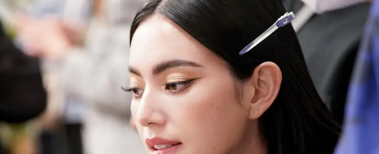 Primer plano de una mujer con ojos rasgados, delineado de gato y cabello oscuro recogido con una pinza.