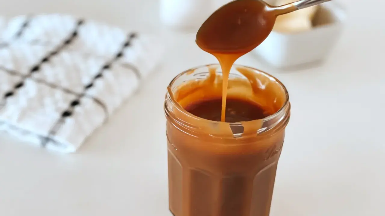Une cuillère verse un caramel beurre salé liquide dans un pot en verre. Parfait pour une recette gourmande.