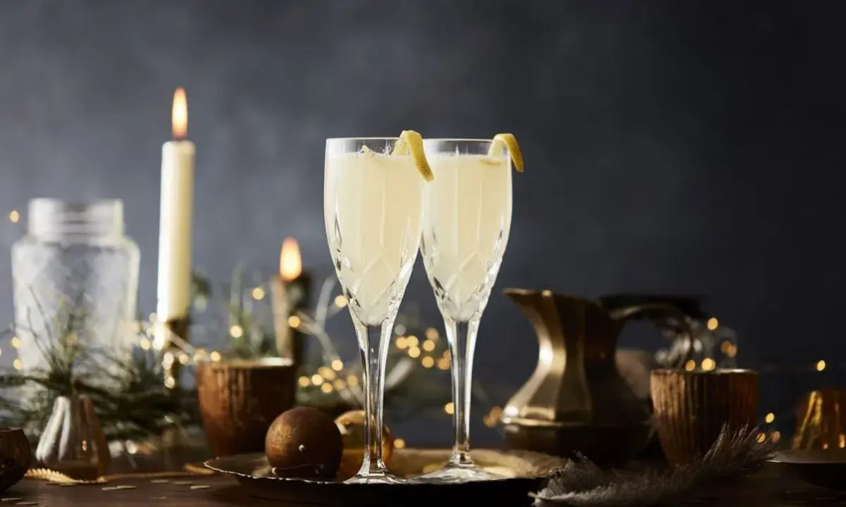 Två eleganta glas med en uppfriskande drink med gin och prosecco, dekorerade med citronskal. Stämningsfull belysning med ljus och ljusslingor skapar en festlig atmosfär.