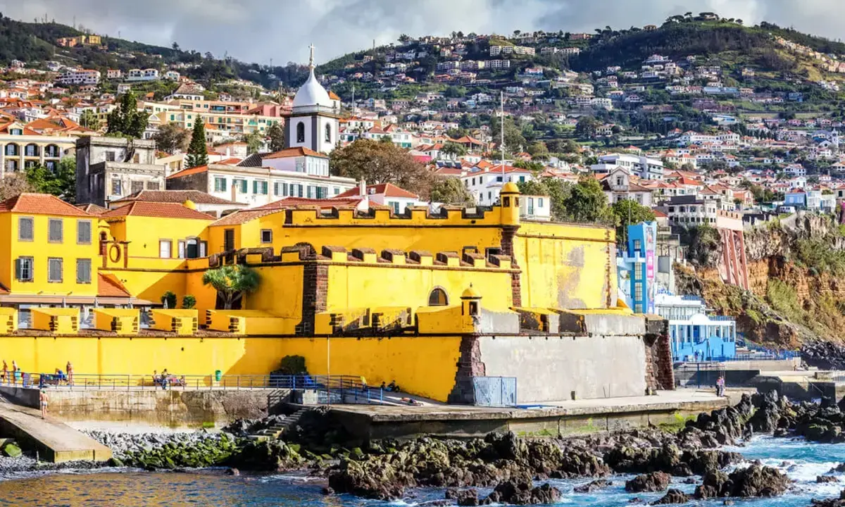 Gelbe Festung in Funchal, Madeira, mit Häusern, die sich den Hang hinaufziehen.