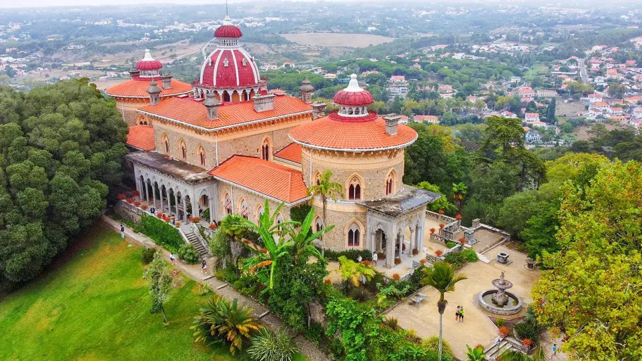 Der Monserrate Palast thront auf einem Hügel, umgeben von üppiger Vegetation und einer malerischen Stadt. Seine roten Dächer und Türmchen sind ein Blickfang.