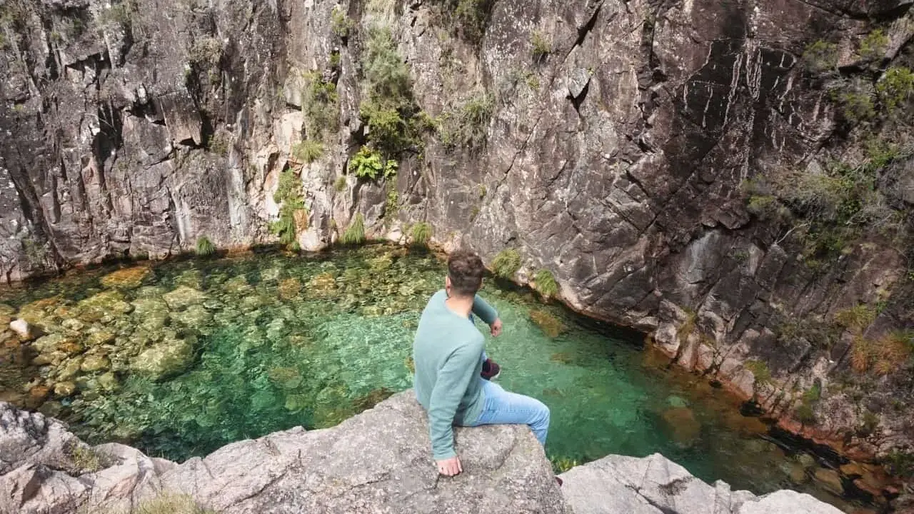 Mann sitzt auf Felsen am kristallklaren Wasser des Peneda-Gerês-Nationalparks.