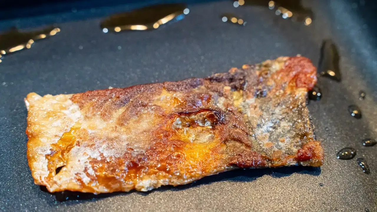 Ein Stück Lachs braten in der Pfanne, die Haut ist knusprig und goldbraun, das Fleisch saftig.