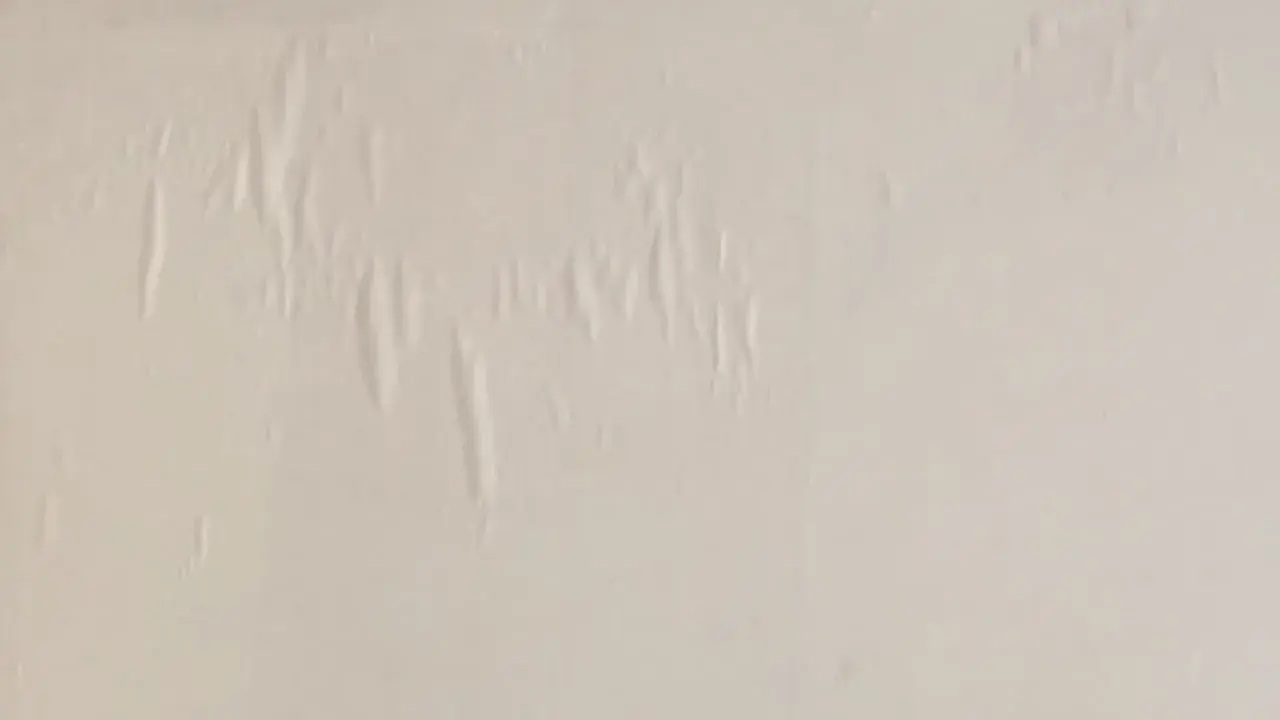 En vit vägg med bubblor och veck i tapeten, som om någon försökt tapetsera på tapet.