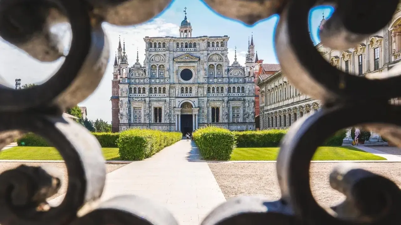 La Certosa di Pavia, un capolavoro rinascimentale, vista attraverso un cancello decorato. Un percorso conduce alla maestosa facciata.
