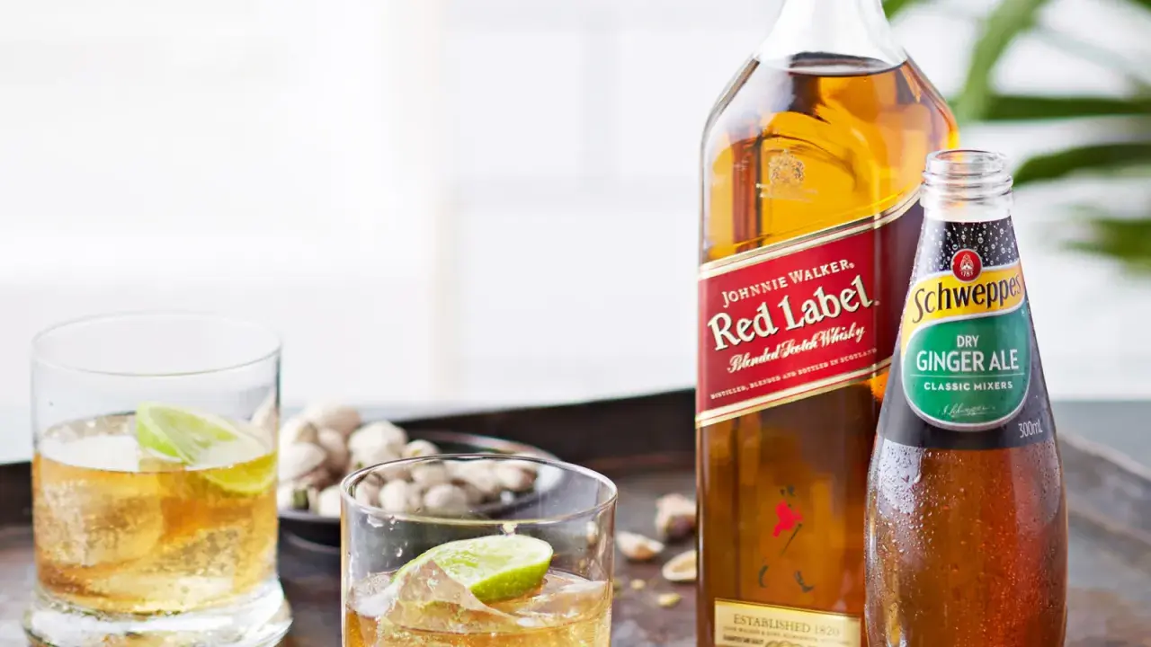 Butelka Johnnie Walker Red Label, butelka Schweppes Ginger Ale i dwa drinki z lodem i limonką.