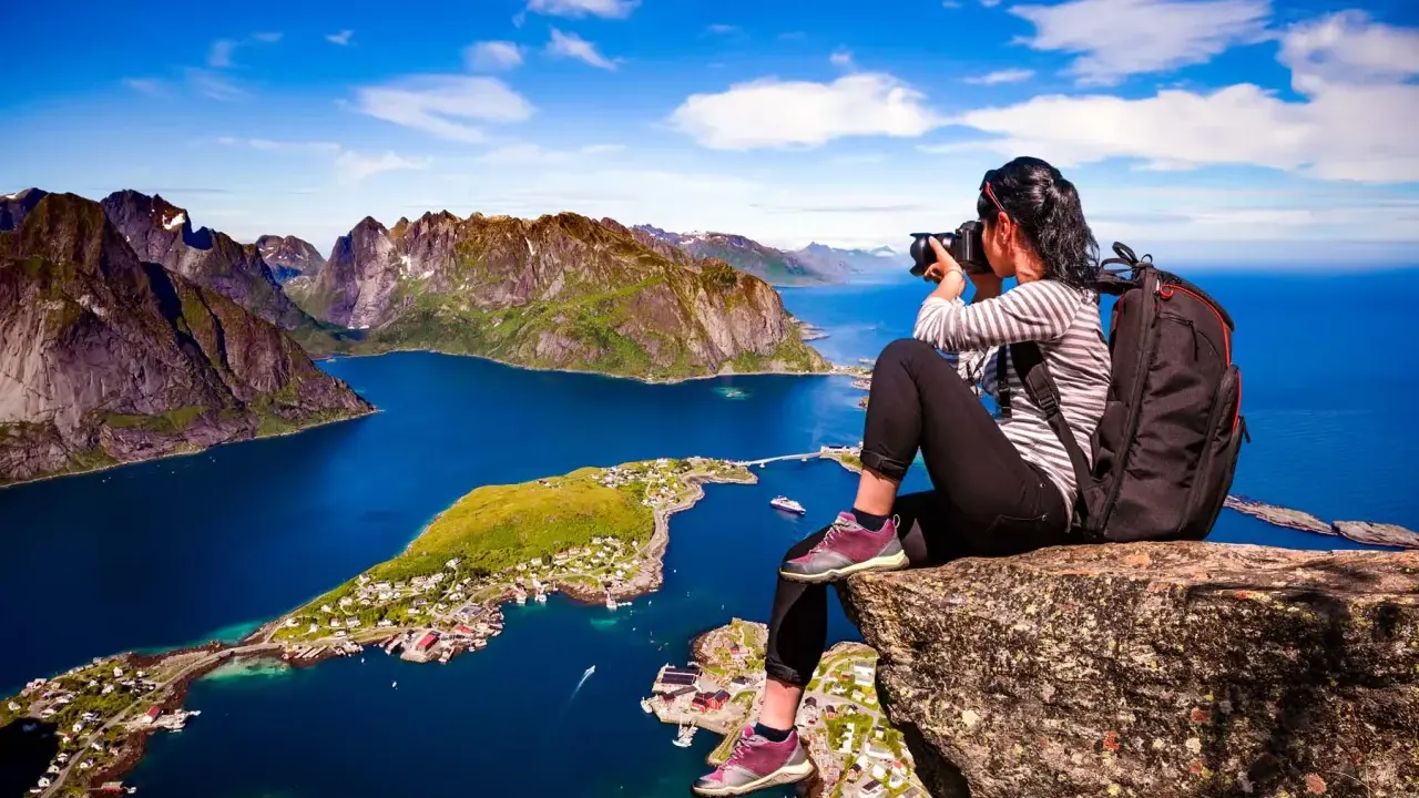 En fotograf fångar de dramatiska vyerna över Lofoten sevärdheter, med branta berg och en idyllisk by vid det blå havet.
