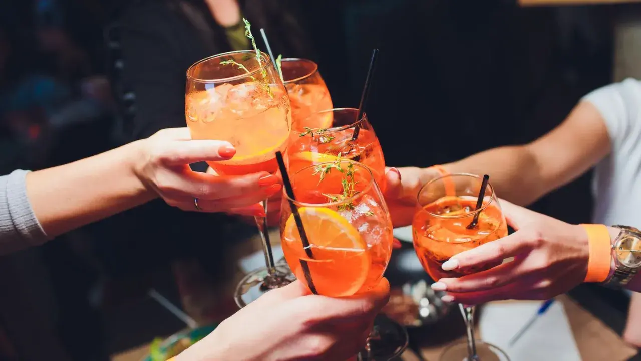 Hände stoßen mit Aperol Spritz an. So einfach wie man ihn macht, so erfrischend ist er!