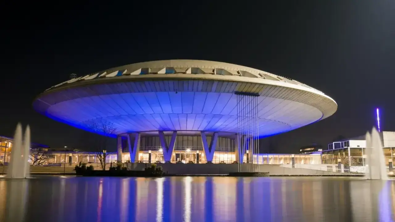 Futurystyczny budynek w Eindhoven, oświetlony niebieskim światłem, z fontannami w stawie. Jedna z głównych eindhoven atrakcji.