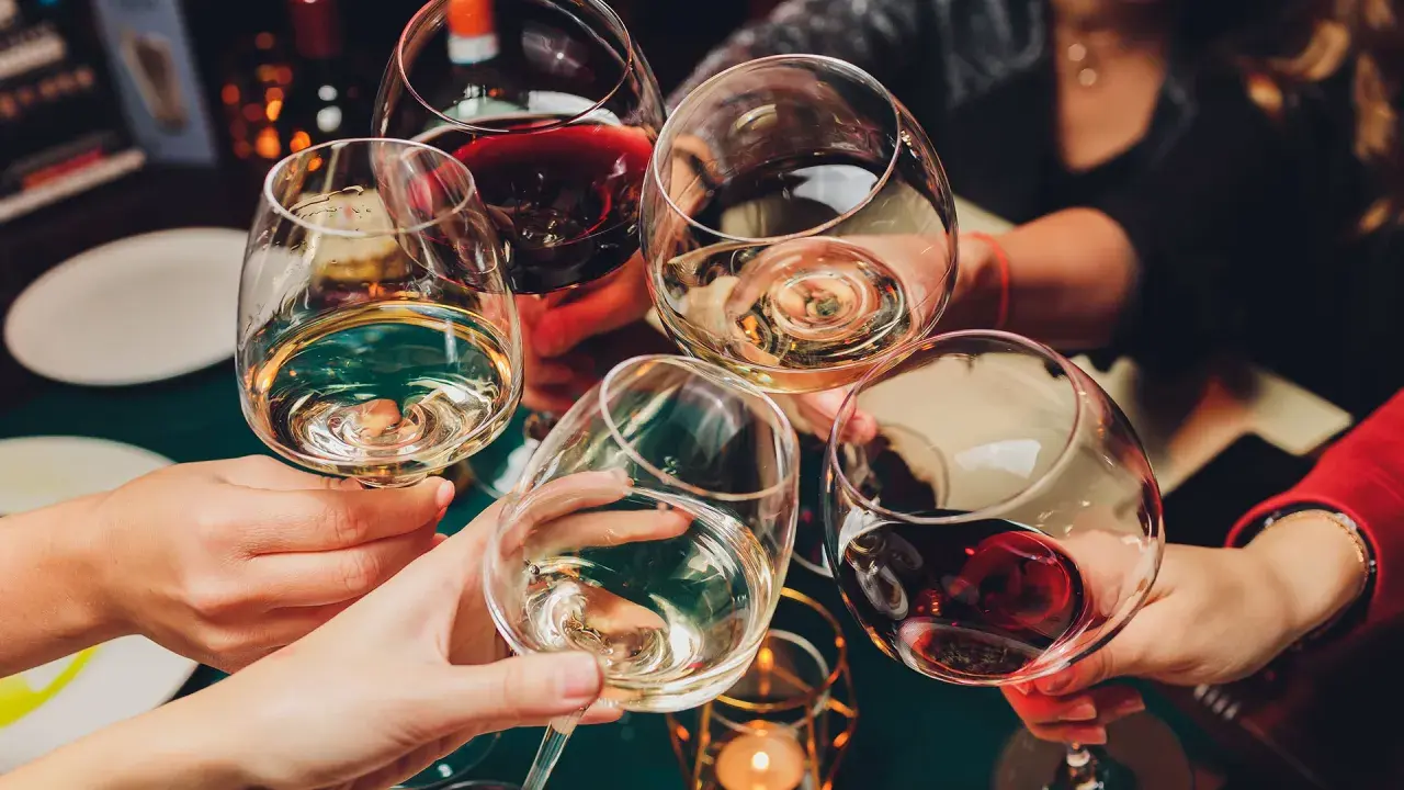 Hände heben Gläser mit Weiß- und Rotwein zum Anstoßen. Die ideale trinktemperatur für den Wein wird genossen.