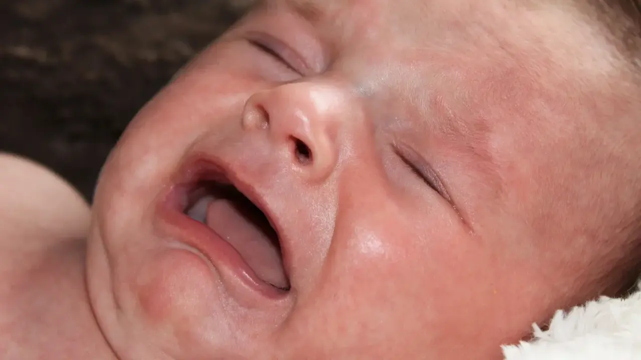 Ett kolikbarn gråter intensivt, med ögonen slutna och munnen öppen.