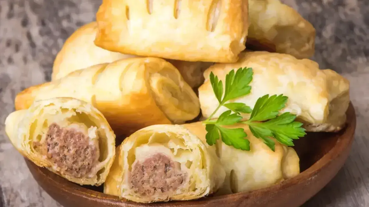 Stos pieczonego ciasta francuskiego z kiełbaską w środku, ozdobiony gałązką pietruszki.