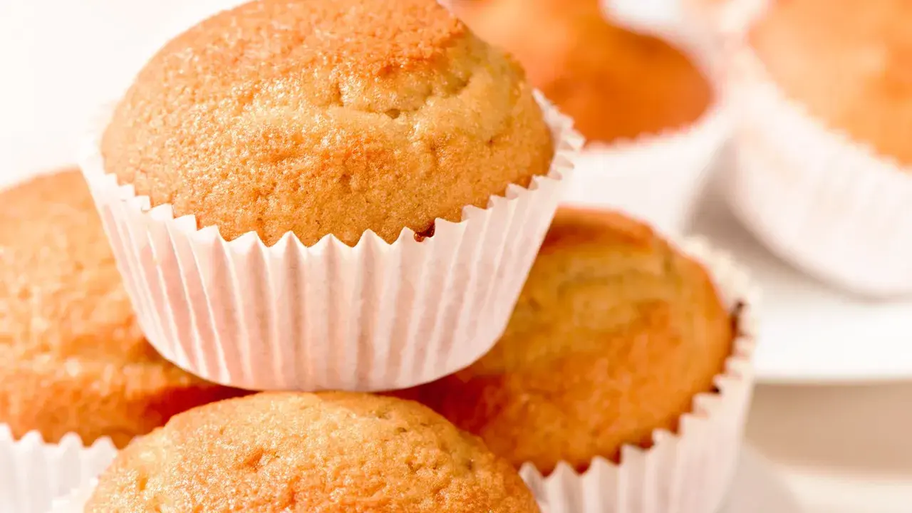 Ein Stapel goldbrauner, veganer Muffins in weißen Papierförmchen. Sie sehen köstlich und frisch gebacken aus.