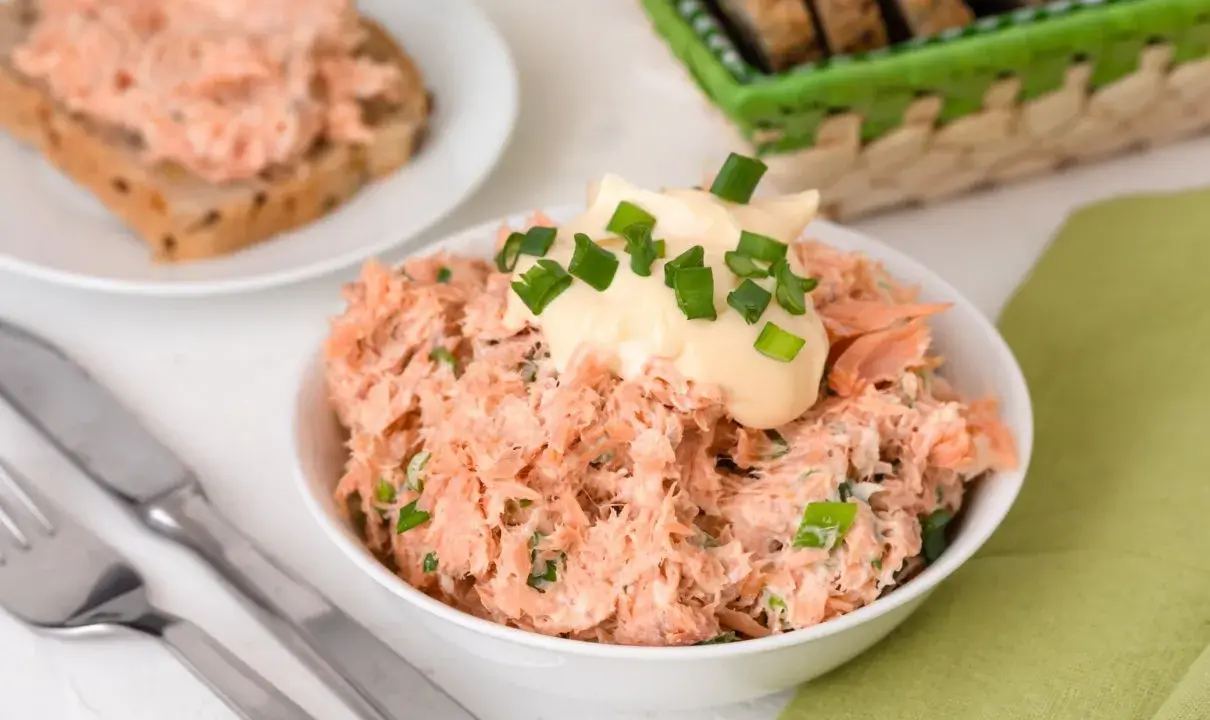 Pyszna pasta z pstrąga wędzonego, udekorowana majonezem i szczypiorkiem, gotowa do podania na chlebie.