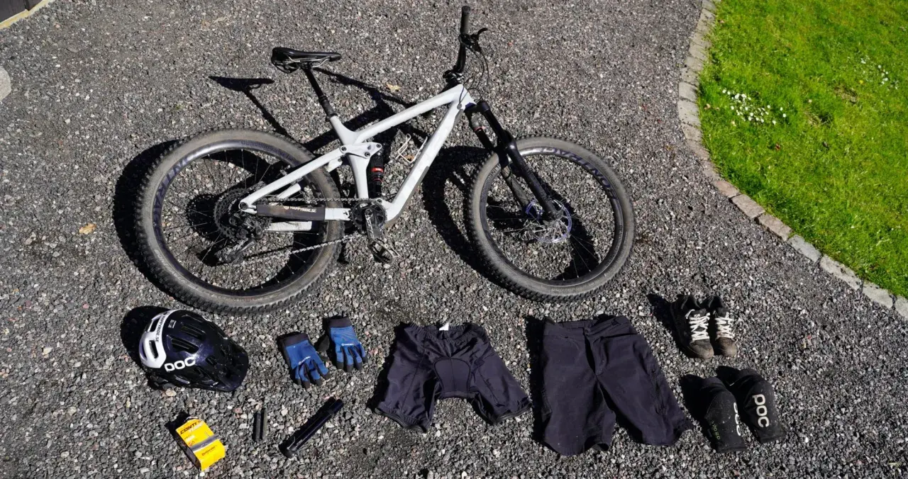 Fullt utrustad för en dag på stigarna: en grå heldämpad cykel, hjälm, handskar, shorts, skor och skydd. Allt för din mtb utrustning.