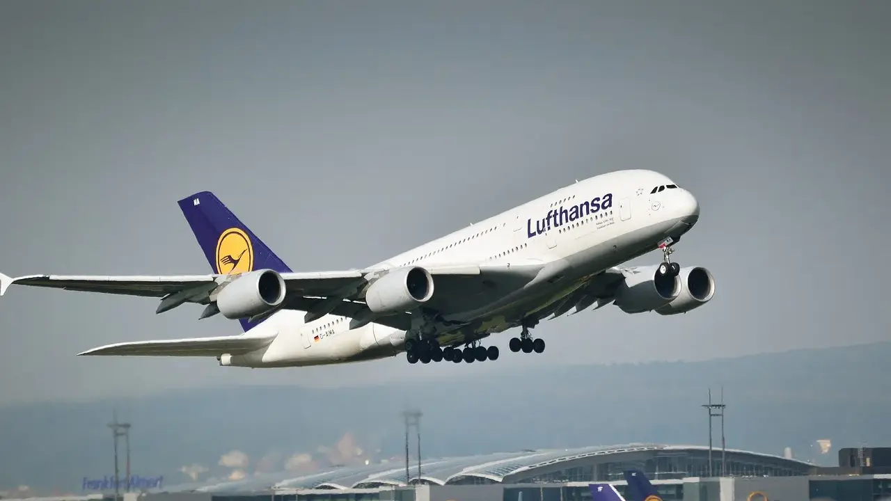 Samolot pasażerski Lufthansa z wysuniętym podwoziem startuje na tle lotniska.