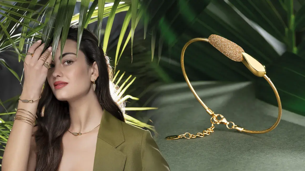 Modella con gioielli Pesavento, tra cui una collana, orecchini e anelli, su sfondo verde con foglie tropicali.