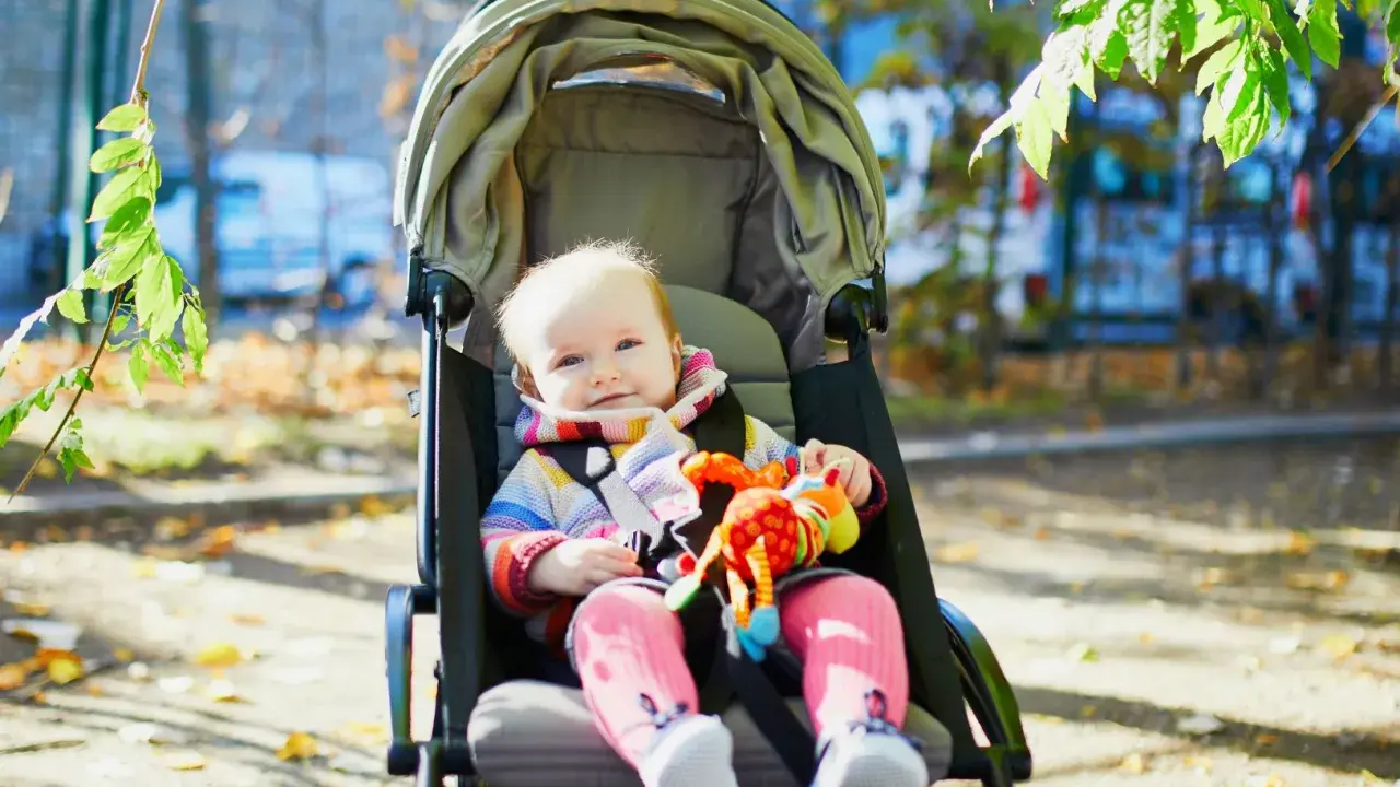 Uśmiechnięte dziecko w kolorowym sweterku i różowych skarpetkach siedzi w spacerówce, trzymając zabawkę. Od kiedy spacerówka stała się jego ulubionym miejscem na świecie.