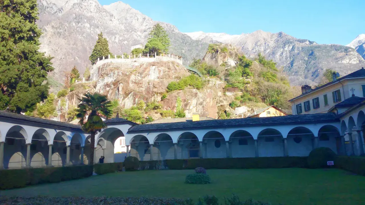 Un porticato ad archi domina un giardino curato, con montagne imponenti sullo sfondo. Un luogo ideale per scoprire cosa vedere a Chiavenna.
