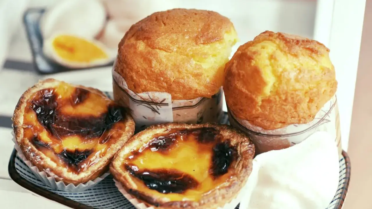 Pyszne portugalskie ciastka, w tym dwa kremowe pastel de nata i dwa muffinki, kuszą apetycznym wyglądem.