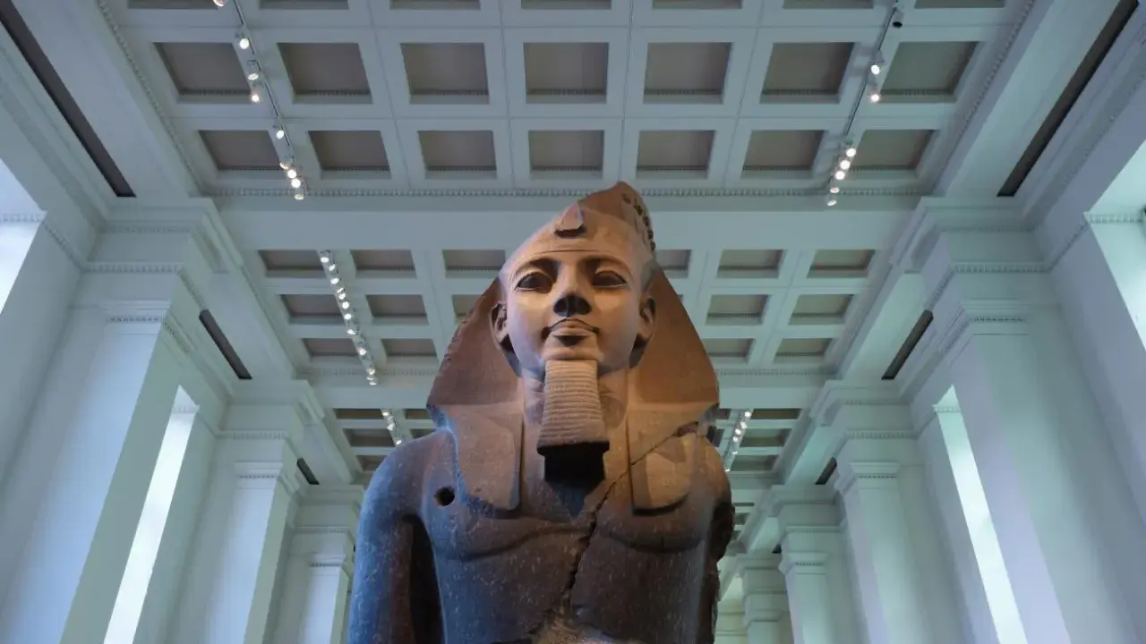 A colossal bust of an ancient Egyptian pharaoh, one of the museum's famous sculptures, stands majestically under a grand, coffered ceiling.
