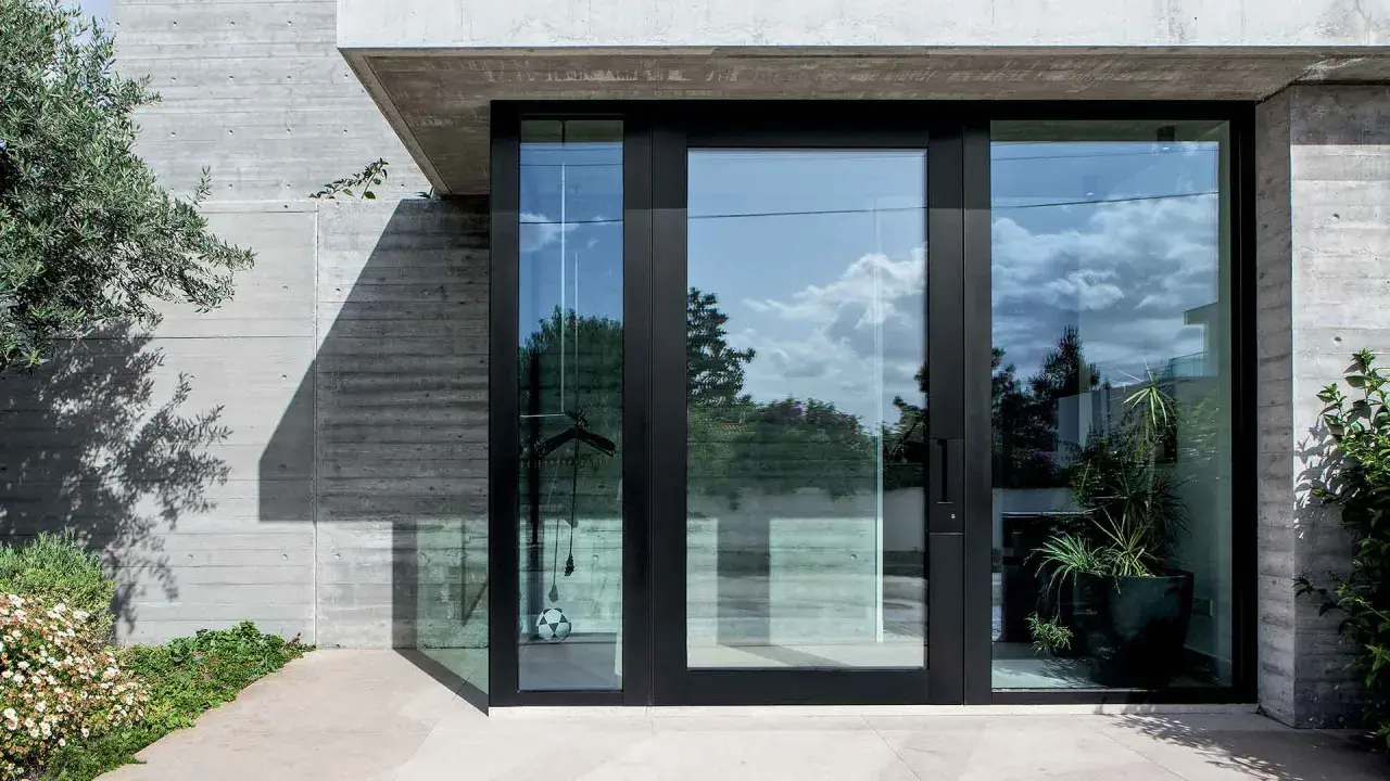 Puerta de entrada moderna con grandes ventanales de cristal, mostrando diferentes tipos de cristales para puertas exteriores que reflejan el cielo y la vegetación.