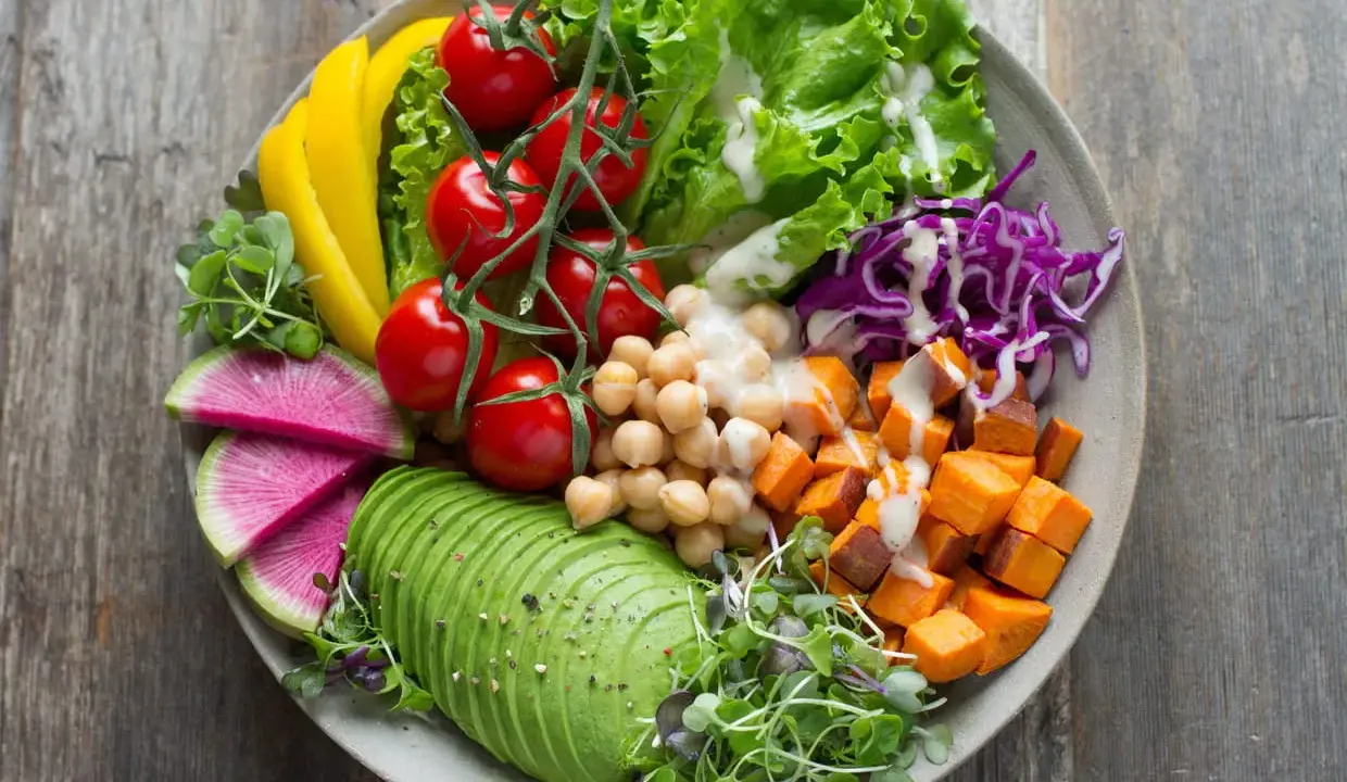 Une salade de crudités colorée et nutritive : avocat, tomates, pois chiches, patates douces, chou rouge, poivron jaune et pousses fraîches.