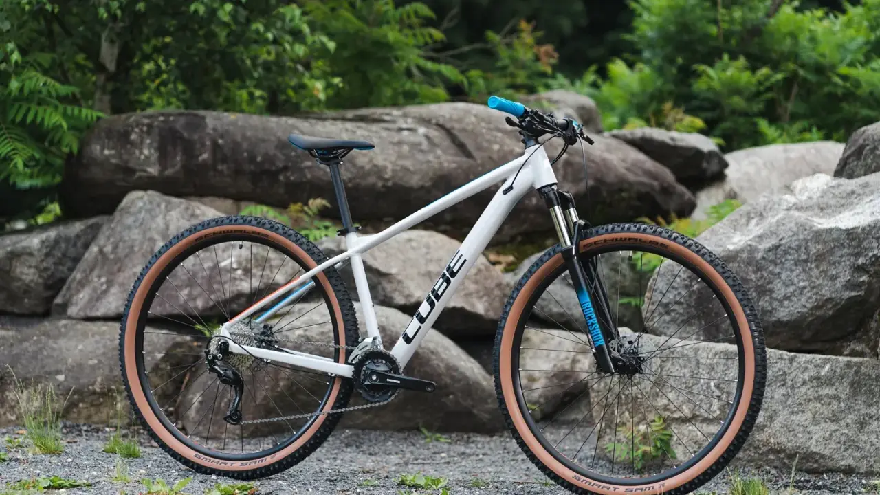 Biały rower Cube z brązowymi oponami, idealny jako rower na długie trasy. Wyposażony w amortyzator RockShox i napęd Shimano.