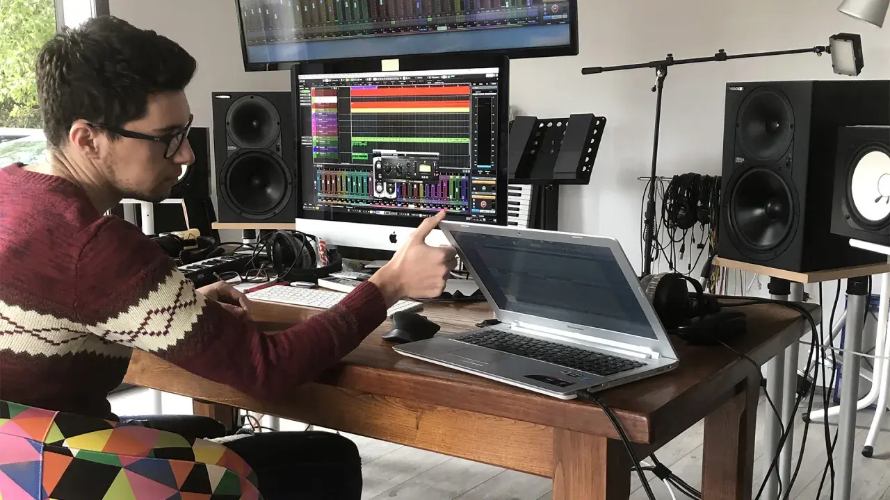 Un jeune sound engineer travaille dans son studio, entouré de matériel audio, d'écrans et d'un clavier.