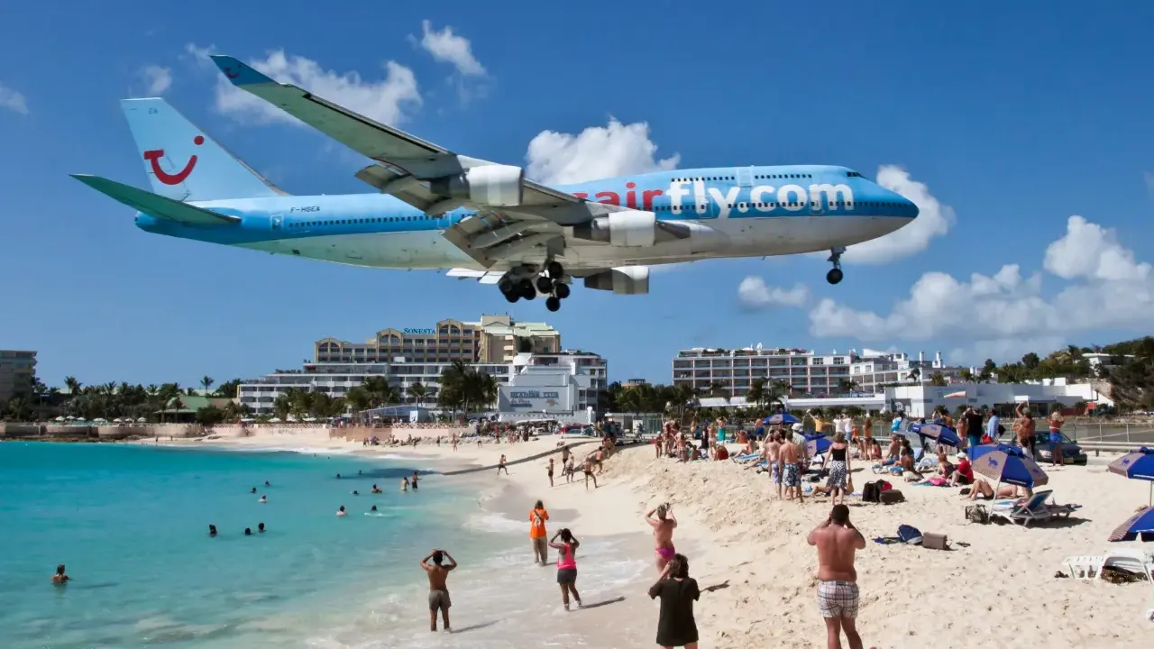 Samolot Airfly.com przelatuje nisko nad plażą pełną turystów, którzy obserwują jego lądowanie.